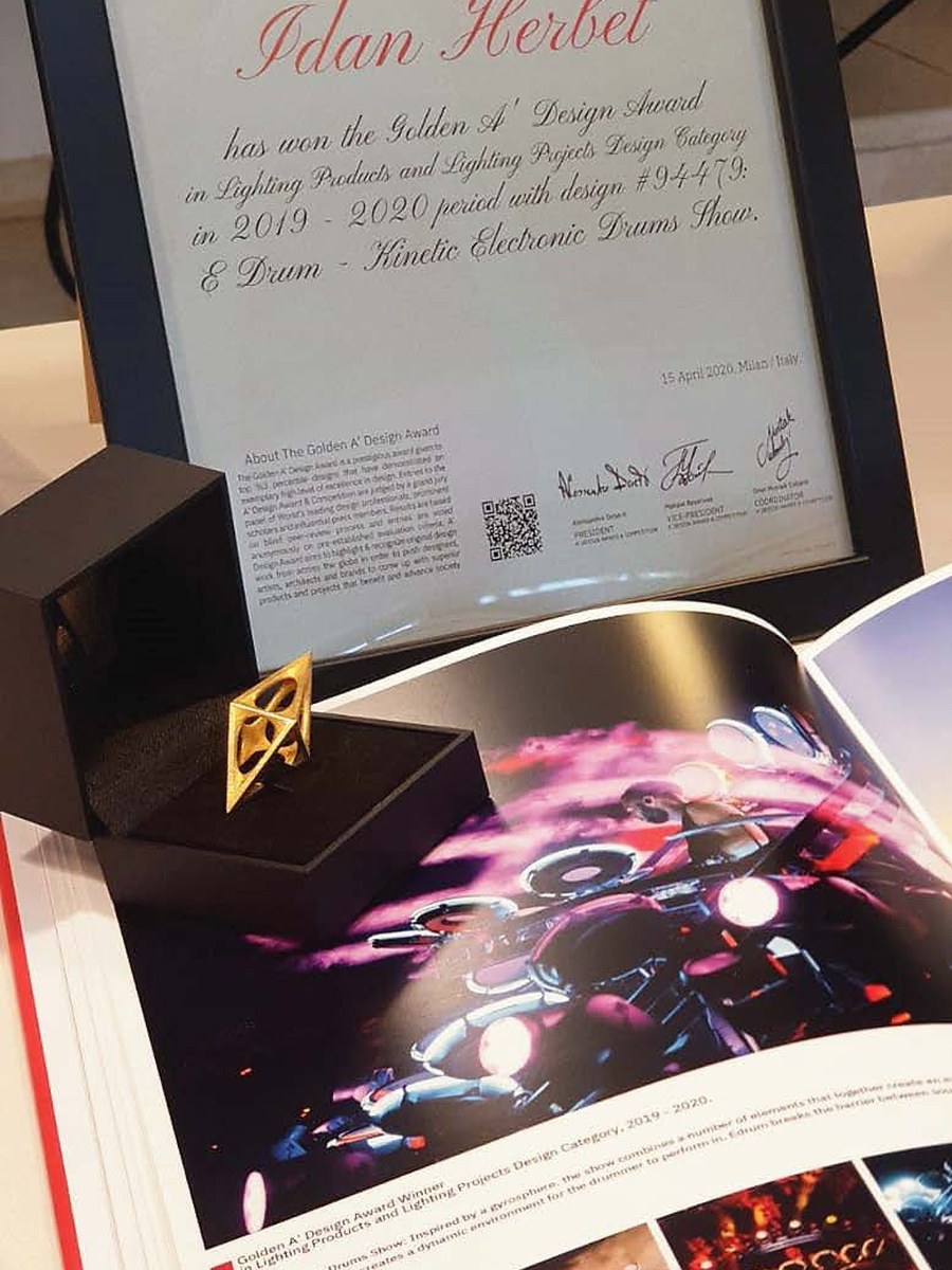 תעודת פרס הזהב של A' Design Award על E-DRUM, ממוסגרת, עם פסלון הפרס ושנתון הזוכים