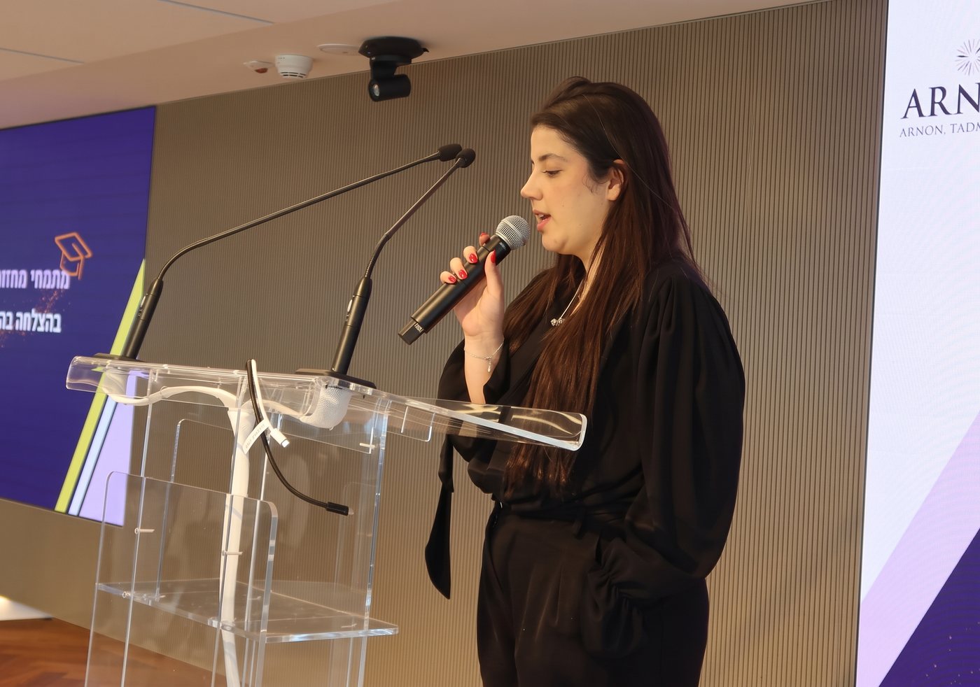 דוברת עם מיקרופון ליד הפודיום, עם שני המיקרופונים על המשטח