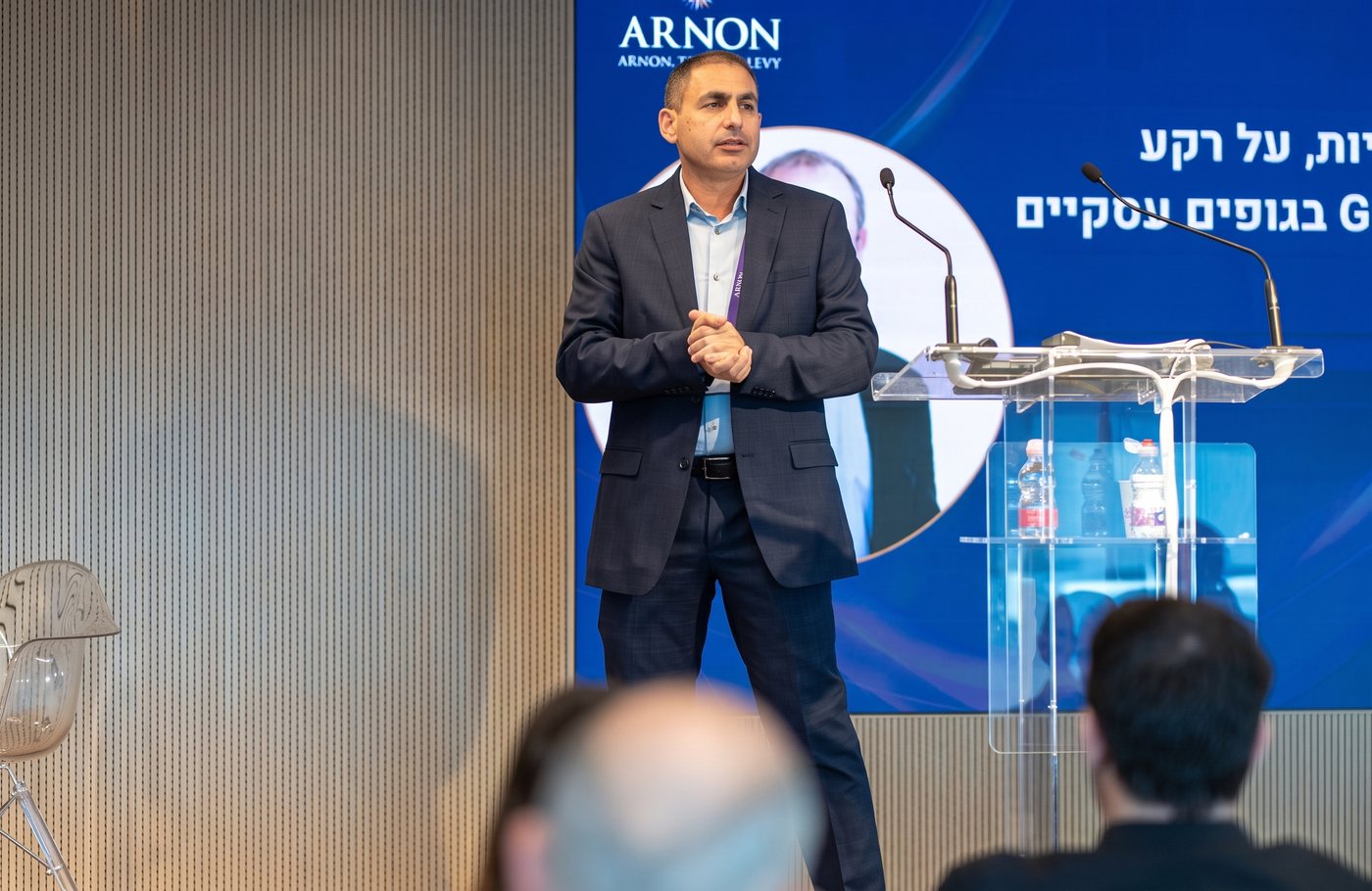 דובר מול המסך, והפודיום עם המיקרופונים והמים לצידו